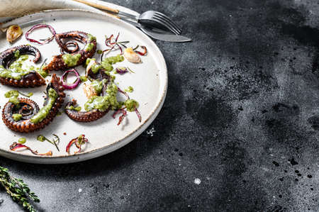 Cooked octopus tentacles with pesto, thyme and onion. Black background. Top view. Copy space.の写真素材