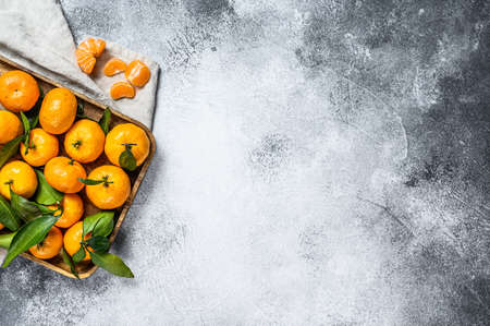 Fresh mandarin oranges fruit or tangerines with leaves in a wooden bowl. Gray background. Top view.の写真素材