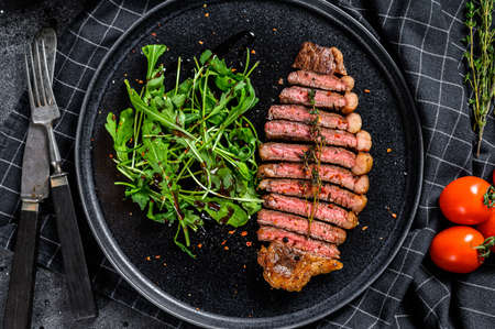Cooked grilled strip loin steak, marbled beef meat with arugula. Black background. Top view.の写真素材