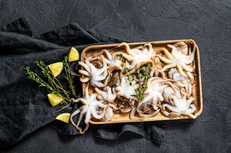Raw baby octopus with thyme and lemon. Organic seafood. Black background. Top view.