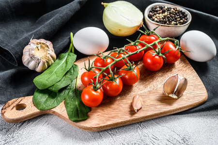 Concept of cooking an omelet with spinach. Ingredients Eggs, onion, garlic, tomatoes, pepper, spinach. Gray background. Top view.の写真素材