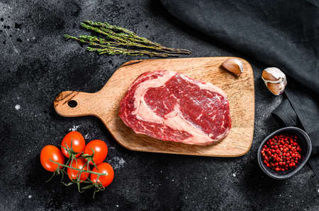 Raw fresh meat Ribeye Steak with seasoning on cutting board. Rib eye beef steak. black background. top view.の写真素材