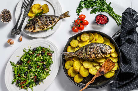 Homemade dinner with baked Dorado fish, arugula salad with tomatoes, baked potatoes. White background. top view.の写真素材
