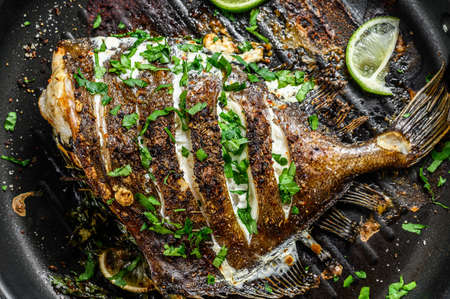 Grilled John Dory fish with lime and parsley in a pan. Gray background. Top view