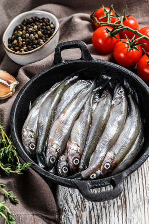 Raw small fish anchovies with pepper and thyme in a pan. White background. Top view.
