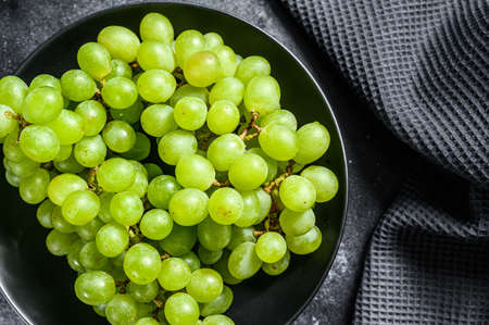 A branch of green juicy grapes in a plate. Black background. Top view.の写真素材