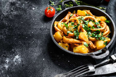 Italian cuisine baked squid with potatoes and tomatoes in a pan. Black background. Top view. Copy space.の写真素材