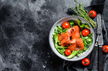 Salad with smoked salmon, arugula, avocado and cherry tomatoes. Concept for a tasty and healthy meal. Black background. Top view. Copy space.の写真素材