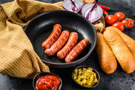 Ingredients for making homemade hot dogs. Sausages in pan, fresh baked buns, mustard, ketchup, cucumbers. Black background. Top view.の写真素材