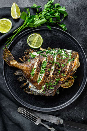 Fried Dory fish with lime and parsley in a pan. Vegatarian health food. Black background. Top view.の写真素材