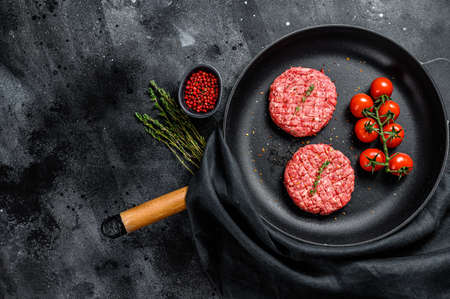 Raw Ground beef meat Burger steak cutlets in a pan. Black background. Top view. Copy space.