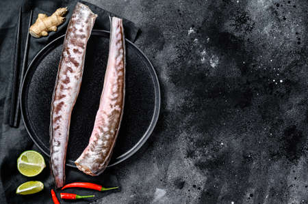 Raw king klip, congrio fish with cooking ingredients, lime, ginger chili pepper. Black background....