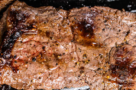 Rump steak in a frying pan. Grilled meat. Black background. Top view.