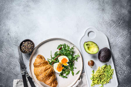 Breakfast, brunch with avacado, arugula, croissant and egg. Gray background. Top view. Space for...