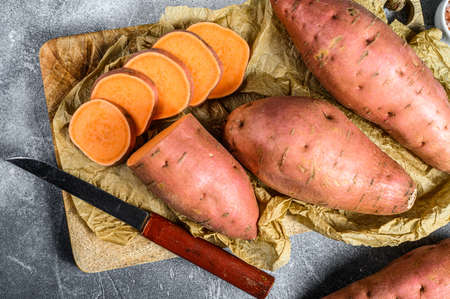Raw sweet potatoes on a chopping Board, organic yam. Farm vegetables. Gray background.