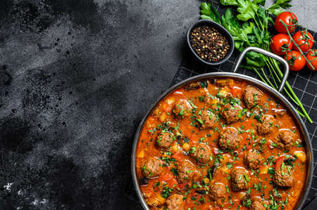 Beef meatballs with tomato sauce and vegetables in a pan. Black background. Top view. Space for...