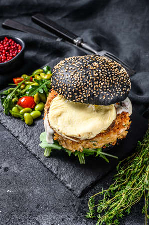 FishBurger with black brioche bun, omelette, fish cutlet and arugula. Black background. Top view.の写真素材