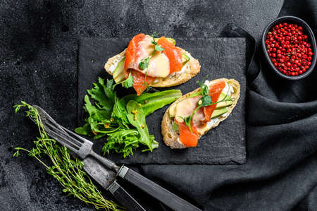 Toasts with avocado and smoked salmon. Black background. Top view.の写真素材