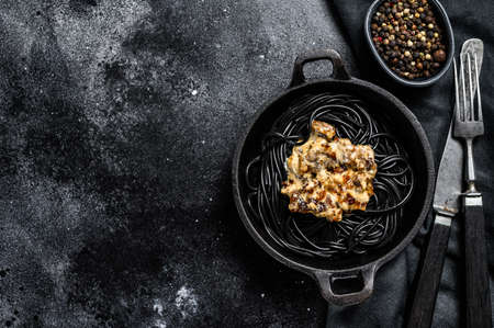 Black spaghetti pasta with squid ink in a pan. Beef in pepper sauce. Black background. Top view. Copy space.の写真素材