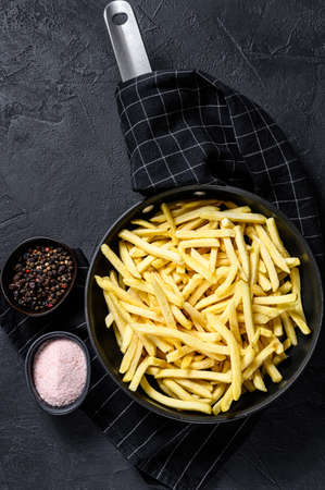 Frozen French fries in a frying pan. Black background. Top view. Space for text.