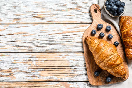 Delicious breakfast with fresh croissants and blueberries. White wooden background. Top view. Copy space.の写真素材