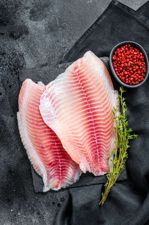Fresh telapia fillet on a chopping Board with thyme. Black background. Top view.