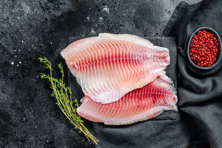 Raw telapia fillet on a chopping Board with thyme and pink pepper. Black background. Top view.の写真素材