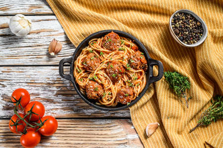 Italian pasta spaghetti with tomato sauce and meatballs in cast iron pan with Parmesan cheese. White wooden background. Top view.の写真素材