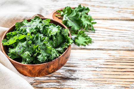 Fresh green superfood kale leaves in wooden bowl. Organic Vegetarian food. White background. Top view. Copy space.の写真素材