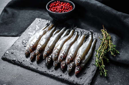 Raw small fish anchovies with pepper and thyme. Black background. Top view.