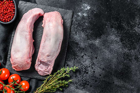 Raw pork tongue with spices and herbs on plate. Black background. Top view. Copy space.