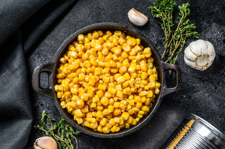 Grains of sweet canned corn in a pan. Black background. Top view.