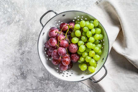 A branch of red and green grapes in a colander. Gray background. Top view.の写真素材