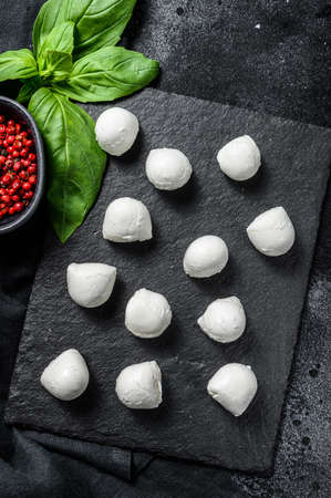 Mini mozzarella cheese balls on a stone Board with Basil leaves and pink pepper. black background. Top view.の写真素材