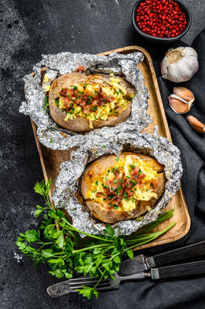 Tasty baked potato topped with cheddar cheese, garlic and parsley. Black background. Top view.の写真素材