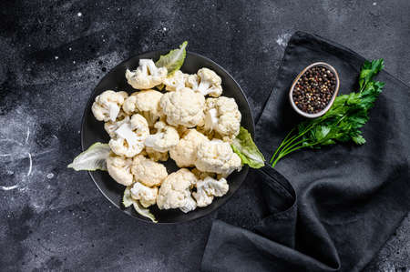 Fresh organic cauliflower cut into small pieces in bowl. Black background. Top view.の写真素材
