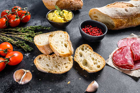 Baguette sandwich ingredients - ham, salami, cheese, butter, tomatoes. black background. top view.の写真素材