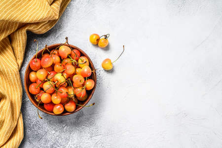 Mix of yellow and red ripe cherries in a bowl. White background. Top view. Copy space.の写真素材