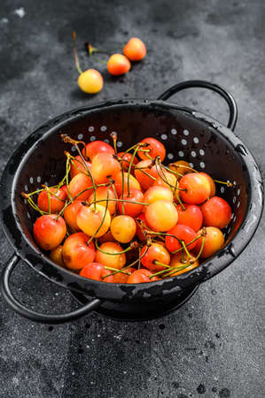 Mix of yellow and red ripe cherries in a colander. Black background. Top view.の写真素材