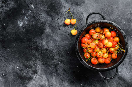 Yellow ripe cherries in a colander. Black background. Top view. Copy space.の写真素材