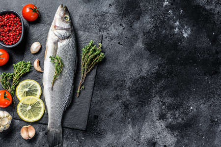 Seabass fish with herbs and lemon, raw sea bass. Black background. Top view. Copy space.の写真素材