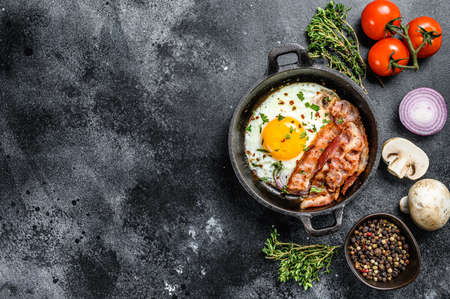 Pan of fried eggs with bacon and fresh tomato. Breakfast set. Black background. Top view. Copy space.の写真素材
