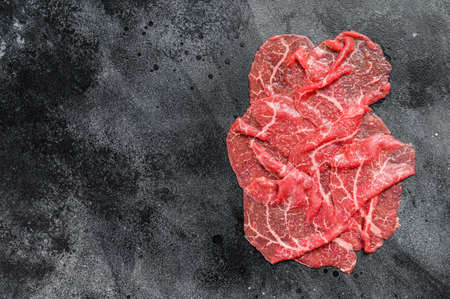 Slices of Beef Capriccio, raw meat. Black background. Top view. Copy space.