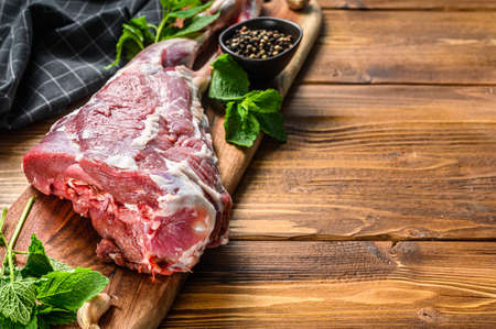 Goat leg with salt and garlic. Raw Farm meat. Wooden background. Top view. Copy space.