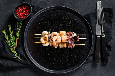 Wooden skewers with shrimp, octopus, squid and mussels. Kebab with seafood. Black background. Top view.の写真素材