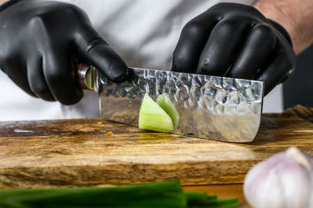 A chef in black gloves is slicing a fresh green cucumber on a wooden chopping Board. Concept of...