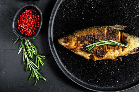 Grilled crucian carp on a white plate. River organic fish. Black background. Top view.の写真素材