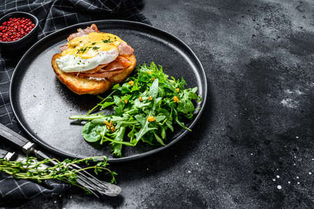 Brioche sandwich with bacon, egg Benedict and hollandaise sauce. Garnish with arugula salad. Black background. Top view. Copy space.の写真素材