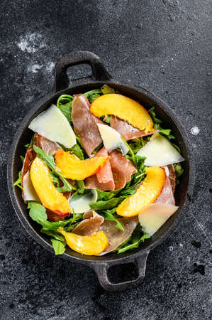 Salad with prosciutto crudo, arugula, peach and Parmesan. Black background. Top view.の写真素材