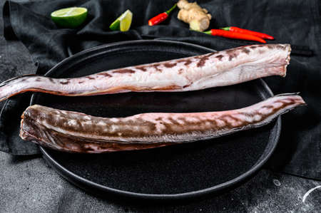 Raw king klip, congrio fish with cooking ingredients, lime, ginger chili pepper. Black background. Top view.の写真素材